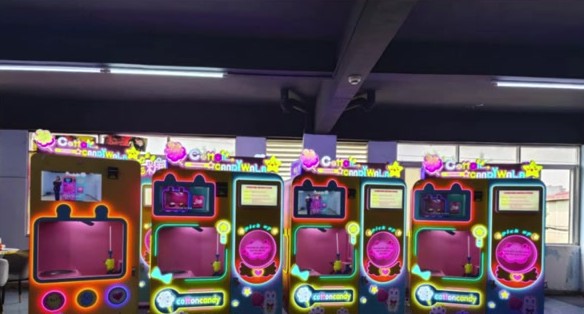 A row of CottonCandyWala cotton candy vending machines with neon-lit cabinets